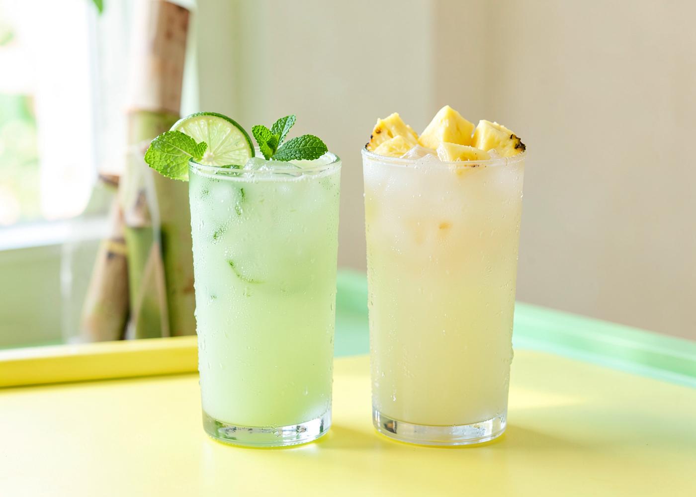 Dois copos gelados de caldo de cana, um com limão e hortelã e outro com abacaxi